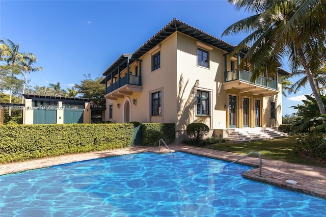 back of house featuring stucco siding, a balcony, a fenced in pool, and a tile roof