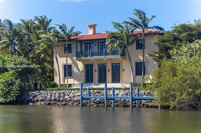 back of property featuring french doors, a water view, a balcony, and stucco siding