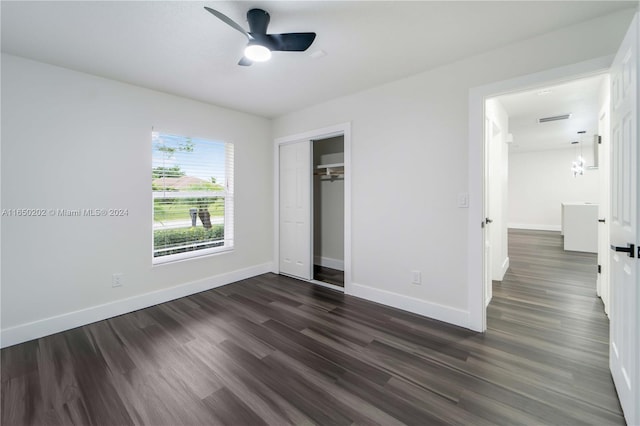 unfurnished bedroom with dark wood-type flooring, a closet, and ceiling fan with notable chandelier