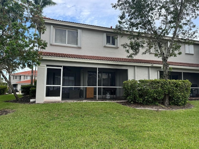 back of property with stucco siding, a lawn, a tiled roof, and a sunroom