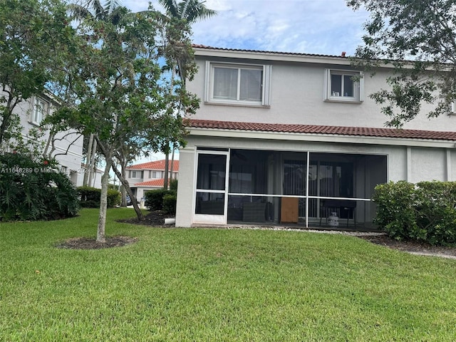 back of house with a yard, a tile roof, stucco siding, and a sunroom