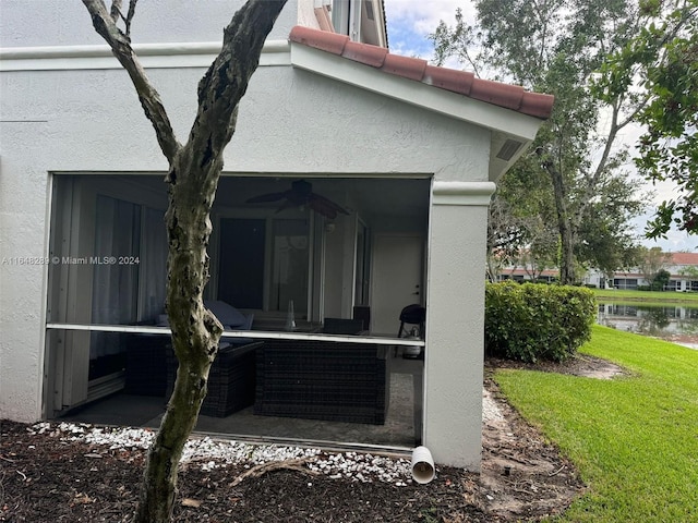 rear view of house featuring a yard, a sunroom, ceiling fan, stucco siding, and a water view