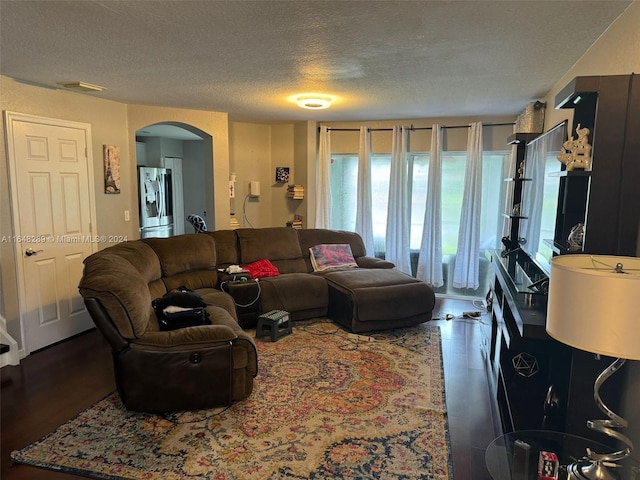 living room featuring wood finished floors, visible vents, arched walkways, and a textured ceiling