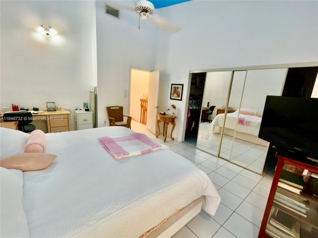 bedroom with a towering ceiling, light tile patterned floors, ceiling fan, and a closet