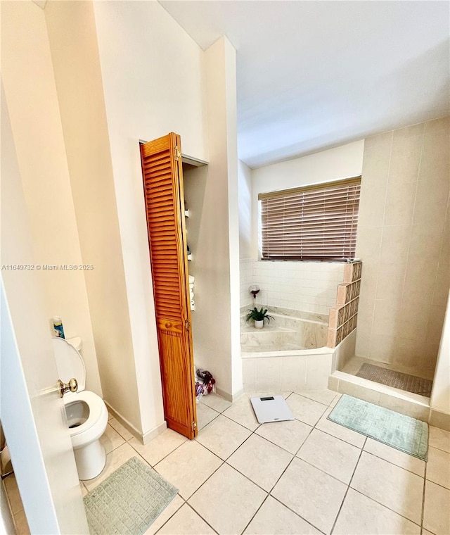 bathroom with tile patterned flooring, tiled tub, and toilet