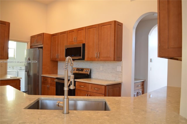 kitchen featuring independent washer and dryer, backsplash, stainless steel appliances, light stone counters, and sink