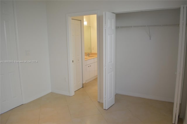 unfurnished bedroom with sink, ensuite bathroom, light tile patterned flooring, and a closet