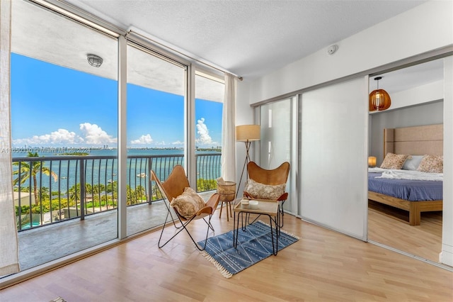 sitting room with light wood-type flooring, a textured ceiling, a water view, and floor to ceiling windows