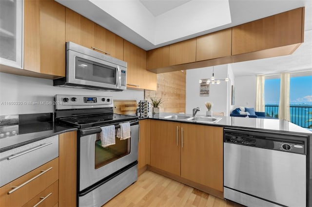 kitchen with light wood-type flooring, appliances with stainless steel finishes, a chandelier, sink, and kitchen peninsula