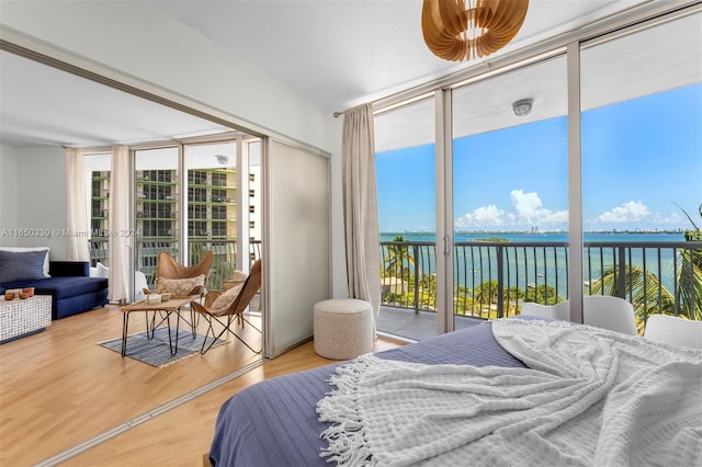 bedroom featuring access to outside, a water view, hardwood / wood-style floors, and expansive windows