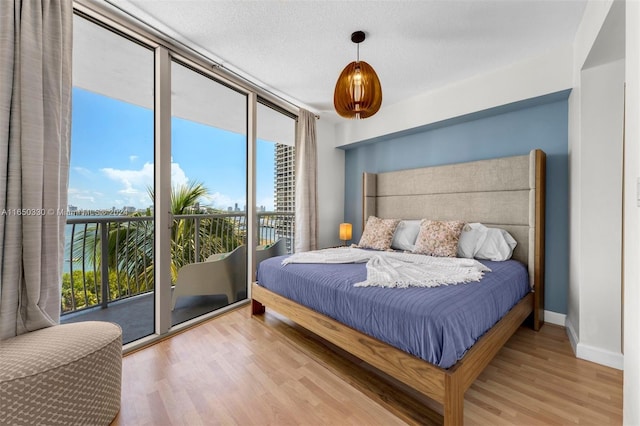 bedroom featuring a wall of windows, a textured ceiling, access to outside, and light hardwood / wood-style flooring