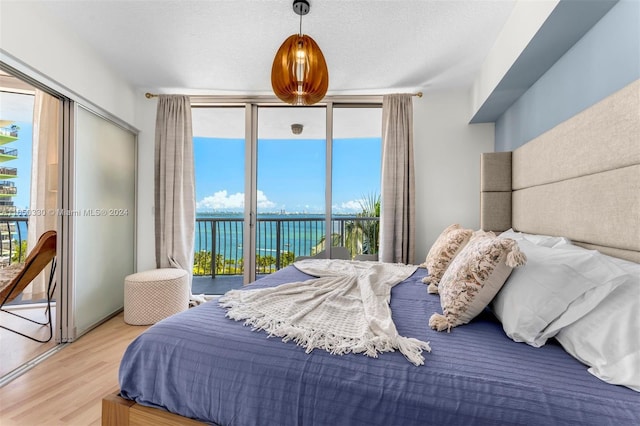 bedroom with a textured ceiling, access to outside, a wall of windows, light wood-type flooring, and a water view