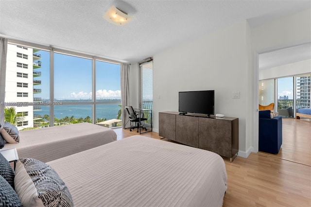 bedroom featuring a wall of windows, light hardwood / wood-style floors, and a textured ceiling