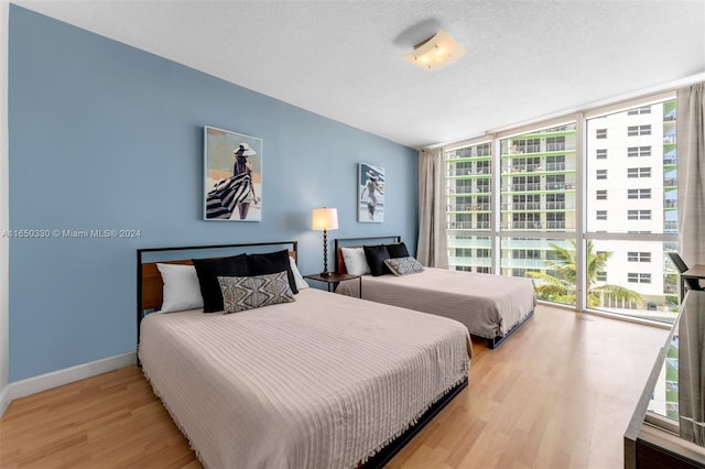 bedroom featuring a textured ceiling, light hardwood / wood-style flooring, and a wall of windows