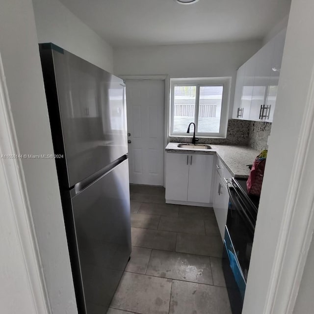 kitchen with white cabinets, tile patterned floors, sink, stainless steel fridge, and black electric range oven