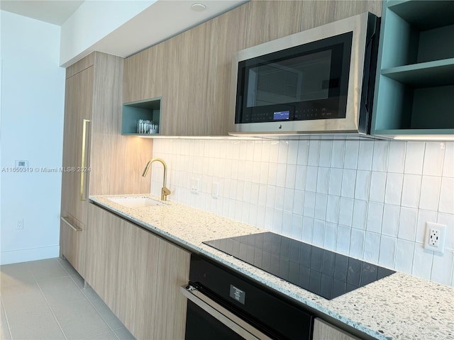 kitchen with light stone countertops, black appliances, backsplash, sink, and light brown cabinets