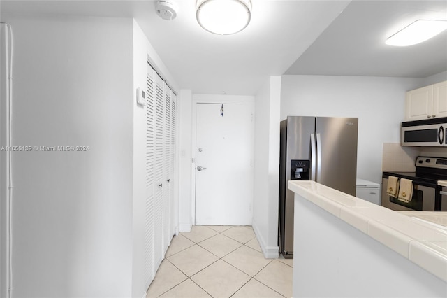 kitchen featuring light tile patterned floors, backsplash, appliances with stainless steel finishes, tile counters, and white cabinets