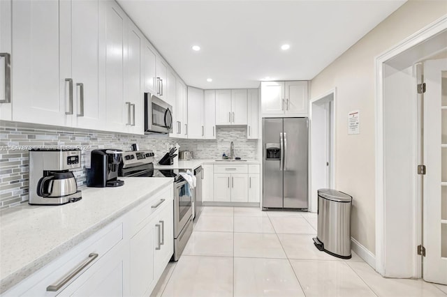 kitchen with appliances with stainless steel finishes, white cabinetry, sink, light tile patterned flooring, and tasteful backsplash