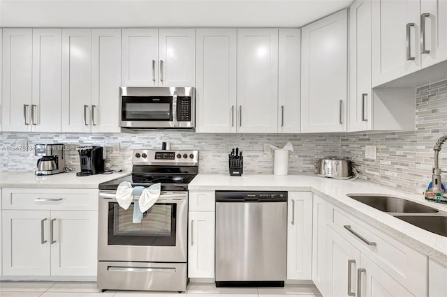 kitchen with backsplash, light tile patterned floors, stainless steel appliances, white cabinetry, and sink