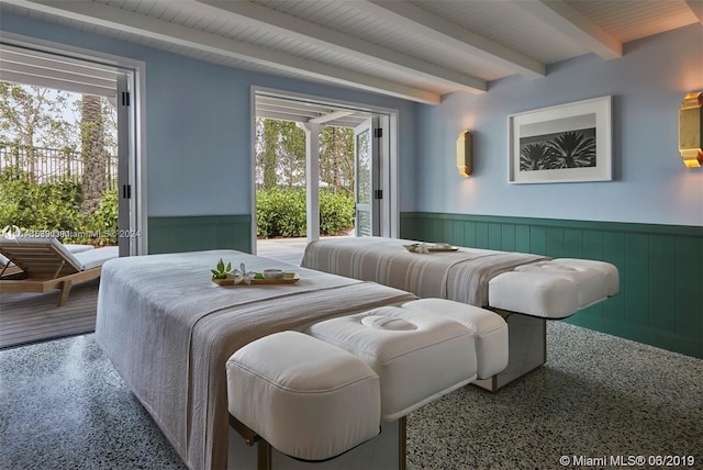 bedroom featuring a wainscoted wall, access to outside, speckled floor, and beamed ceiling