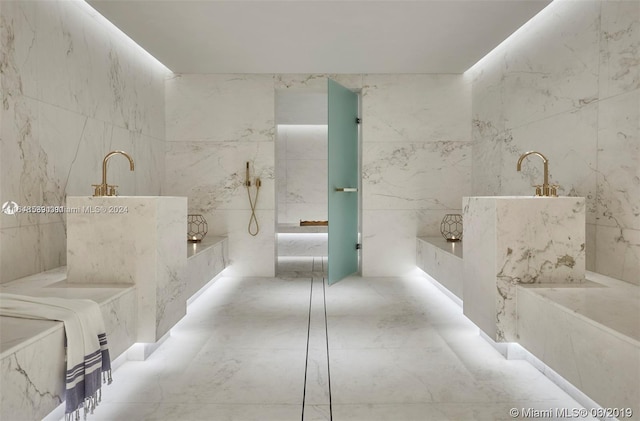 bathroom with marble finish floor, stone wall, and a tub with marble appearance