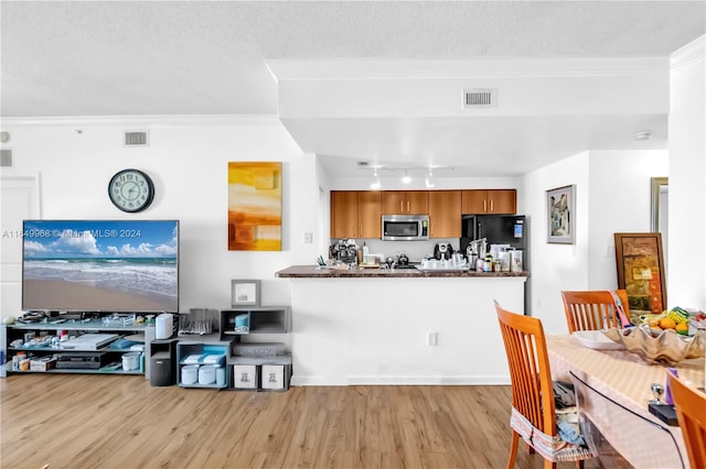 kitchen with light hardwood / wood-style floors, a textured ceiling, black refrigerator, and ornamental molding