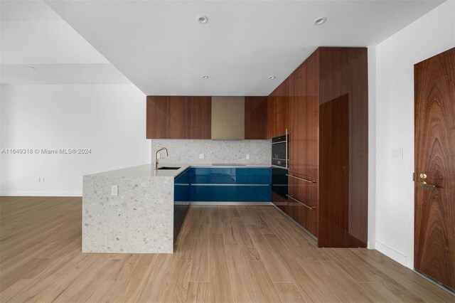 kitchen featuring black appliances, light stone counters, kitchen peninsula, decorative backsplash, and light hardwood / wood-style floors