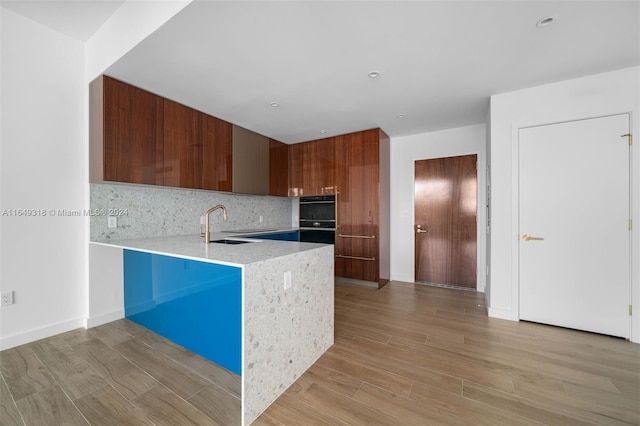 kitchen featuring backsplash, light wood-type flooring, sink, kitchen peninsula, and double oven