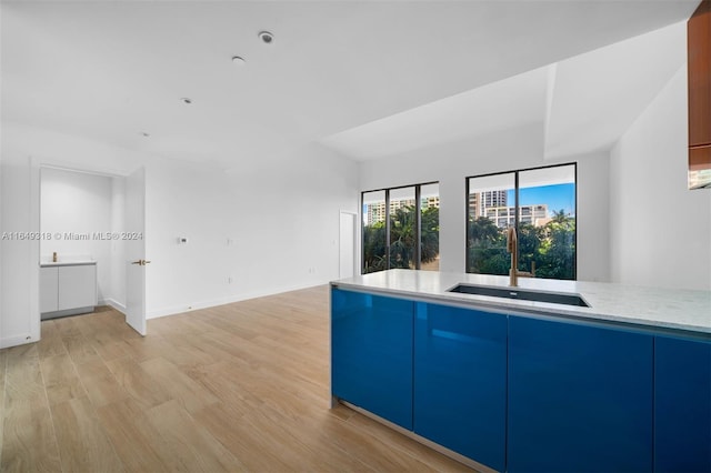 kitchen with light wood-type flooring, light stone counters, blue cabinetry, and sink