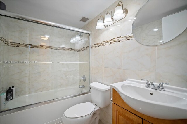 full bathroom featuring vanity, tile walls, toilet, and bath / shower combo with glass door