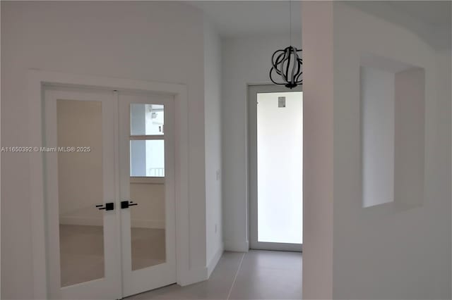 hallway featuring light tile patterned floors, a notable chandelier, and french doors