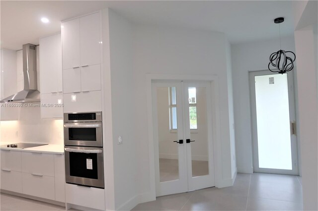 kitchen featuring pendant lighting, wall chimney range hood, white cabinetry, and stainless steel double oven