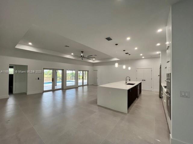 kitchen featuring french doors, sink, a tray ceiling, an island with sink, and white cabinets