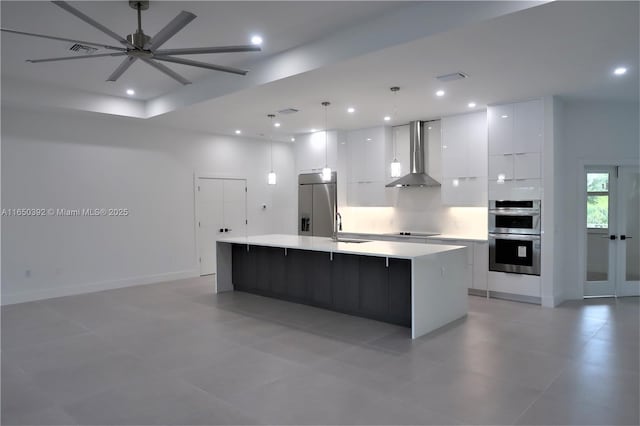 kitchen with appliances with stainless steel finishes, pendant lighting, white cabinets, a large island with sink, and wall chimney exhaust hood