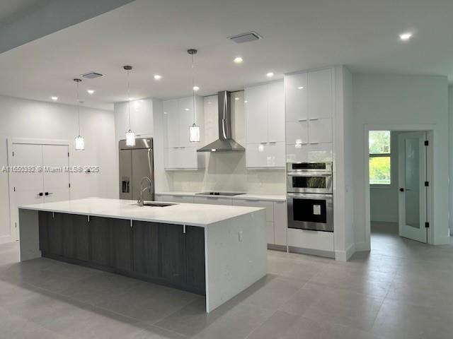 kitchen with a large island, wall chimney range hood, decorative light fixtures, and stainless steel appliances