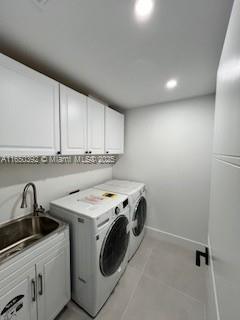 clothes washing area with separate washer and dryer, sink, and cabinets