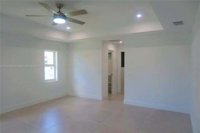 unfurnished room with a raised ceiling, ceiling fan, and light tile patterned flooring