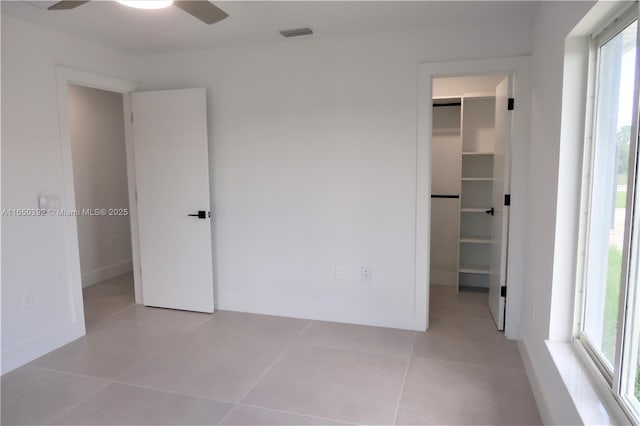 unfurnished bedroom with light tile patterned floors, a walk in closet, a closet, and ceiling fan