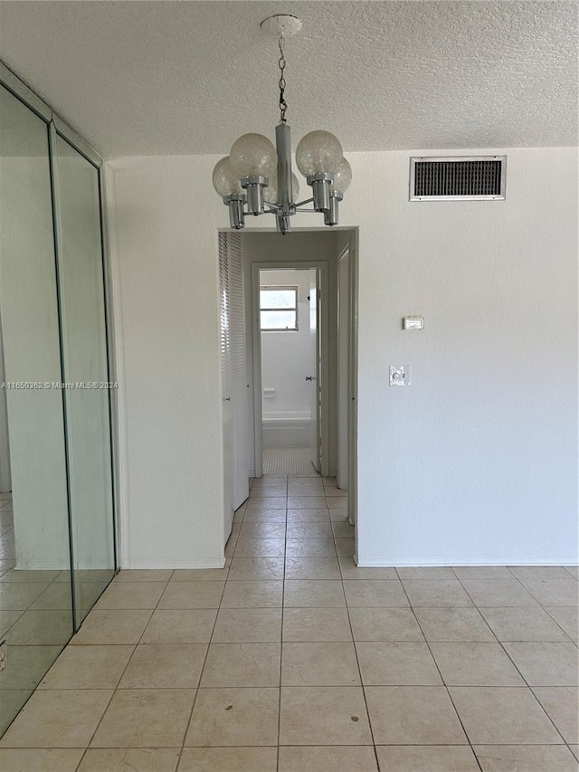 hallway with light tile patterned floors, a chandelier, and a textured ceiling