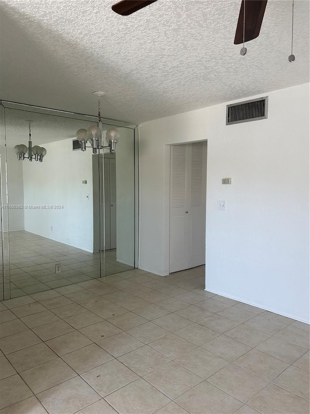 unfurnished room with a textured ceiling, light tile patterned floors, and ceiling fan with notable chandelier