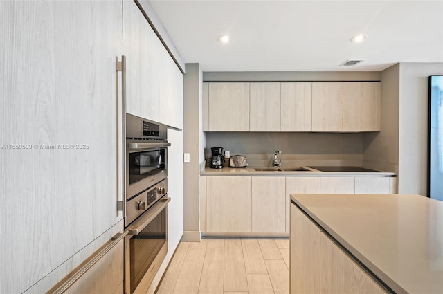 kitchen with black electric cooktop, sink, oven, and light brown cabinetry