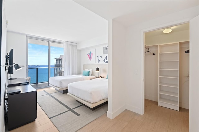 bedroom featuring expansive windows, a walk in closet, access to exterior, and light hardwood / wood-style flooring