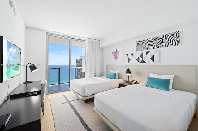 bedroom featuring a water view, a wall of windows, access to exterior, and light hardwood / wood-style floors