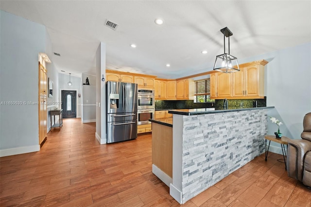 kitchen with appliances with stainless steel finishes, decorative light fixtures, decorative backsplash, and kitchen peninsula