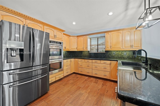 kitchen featuring stainless steel appliances, light wood-type flooring, dark stone counters, pendant lighting, and sink