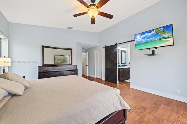 bedroom featuring ensuite bathroom, ceiling fan, a barn door, and hardwood / wood-style flooring