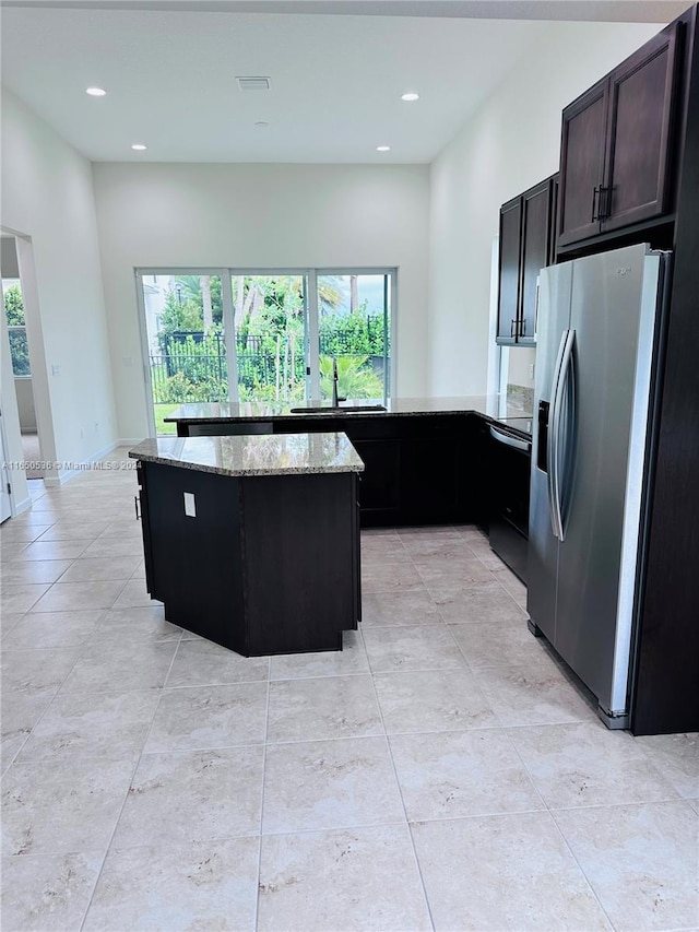 kitchen with a center island, light stone counters, sink, dark brown cabinets, and stainless steel fridge with ice dispenser