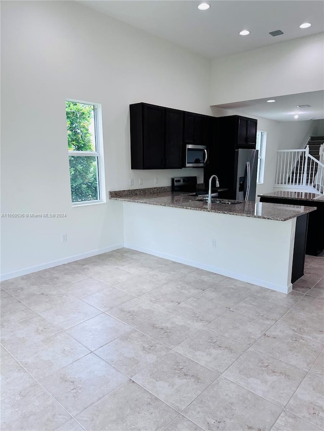 kitchen featuring kitchen peninsula, dark stone countertops, sink, and stainless steel appliances