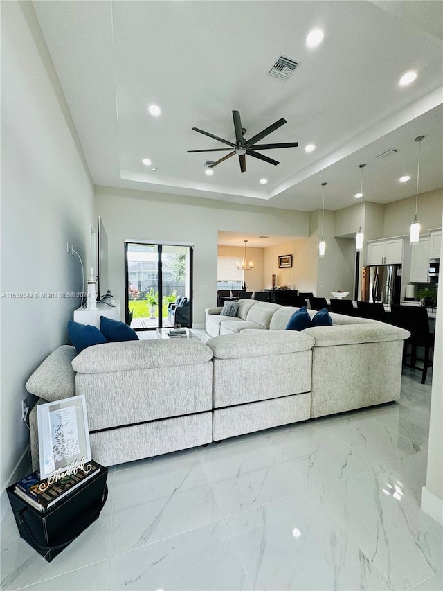 living room with a tray ceiling and ceiling fan with notable chandelier