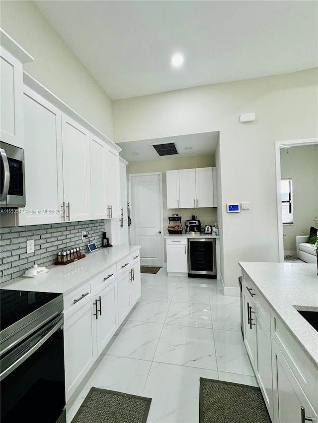 kitchen featuring white cabinets, appliances with stainless steel finishes, light stone counters, and beverage cooler